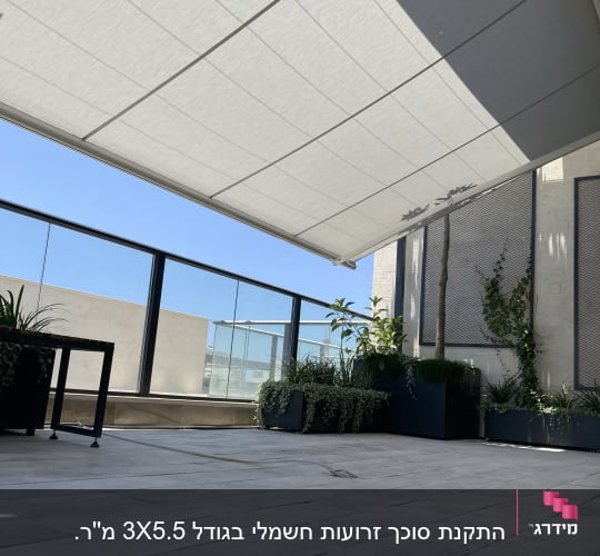 סוכך זרועות מתקפל מתוח מעל מרפסת מרוצפת עם מעקה זכוכית